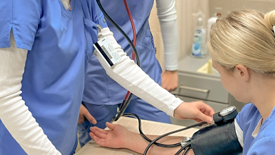 A person in blue scrubs taking another person’s blood pressure in a clinical setting.