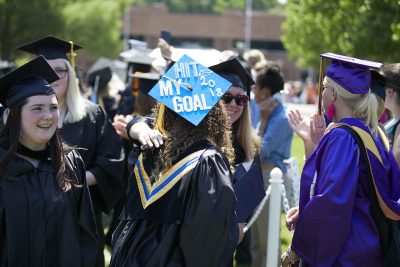 Recent DCCC graduates hug with top of cap reading "Hit my goal 2018"