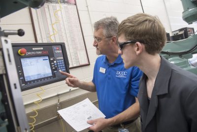 Instructor shows student how to use machine equipment.