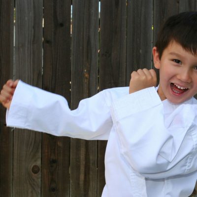 young karate student in white uniform in fighting stance and smiling at camera