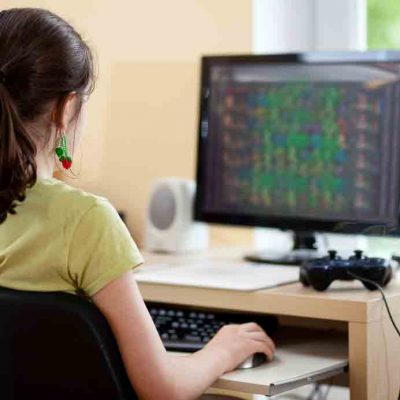 Student in front of computer screen with gaming controller laying on desk