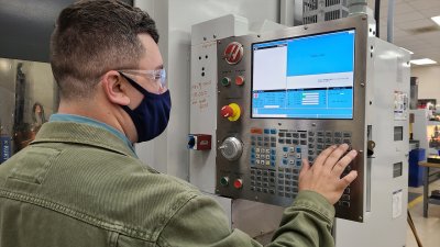 Computer Integrated Machining student in mask operates keypad of equipment