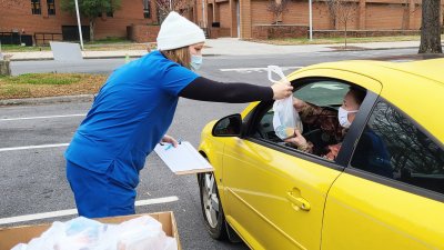 Volunteer handing bag of medicine to driver of yellow car