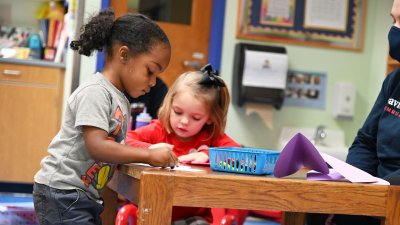 Two preschoolers color cards at wooden table