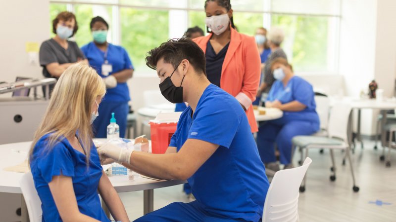 Student in scrubs prepares the arm of another student as they practice immunization administration