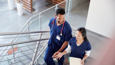 Two nurses in blue scrubs climbing a flight of stairs