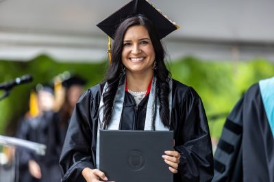 Graduate in cap and gown holds up diploma