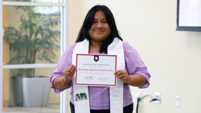 Student with white graduation stole holds certificate