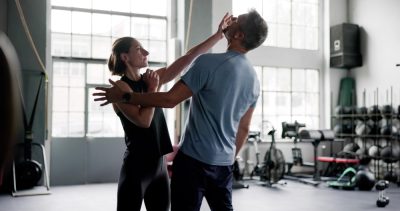 Two people practicing self-defense in a gym.