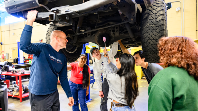 Automotive Students and Instructor look underneath car.