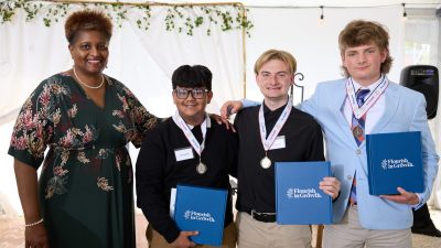 From left to right are Dr. Dee Stokes, director of the Small Business Center at Davidson-Davie Community College, with YES winners John Vasquez (second place), Davis Norton (first place), and Caswell Moore (third place). Text on the folders in the winner's hands reads: "Flourish in Growth"