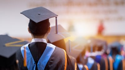 Graduates in caps and gowns at a ceremony, with one central figure in focus from behind.