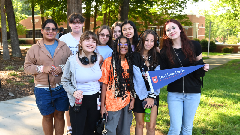 Group of Davidson-Davie students in a campus courtyard holding a pennant with the Davidson-Davie Community College logo.