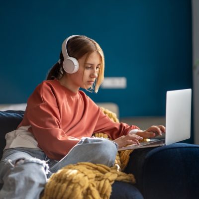 Person wearing headphones sitting on a couch using a laptop.