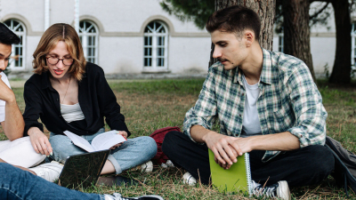 Students sitting on grass with books and notebooks.
