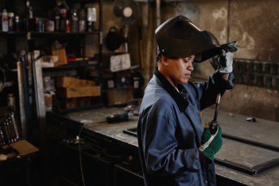 Side view portrait of woman welder inspecting tools in industrial workshop