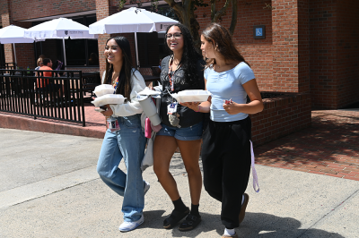 Three women walking with takeout containers on a college campus.