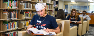 People reading in a library with bookshelves and lounge chairs.