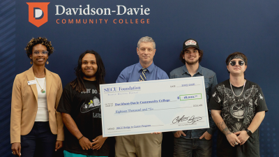 Five people stand with a large check in front of a backdrop reading "Davidson-Davie Community College."