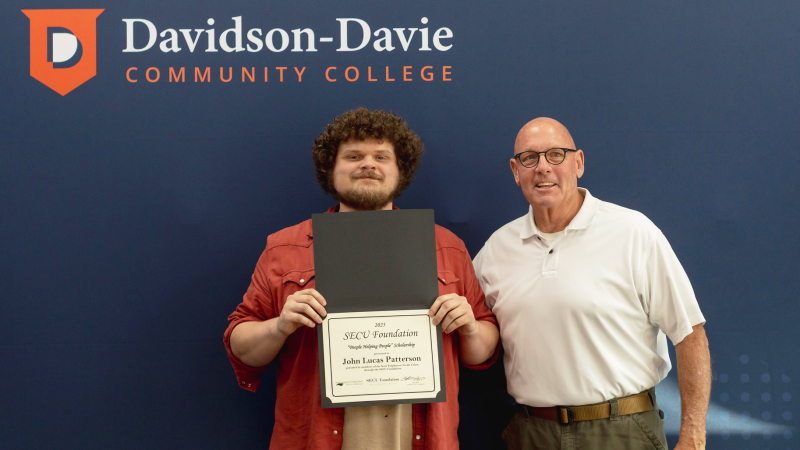 Two men standing with a certificate in front of a Davidson-Davie Community College backdrop.