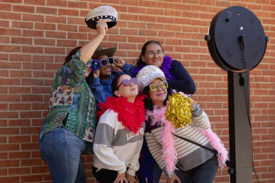 A group of five people in colorful costumes posing for a photo booth in front of a brick wall.