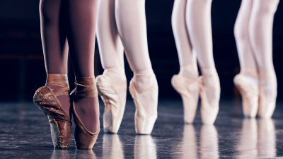 Close-up of ballet dancers' feet on pointe in a row on a dance floor.