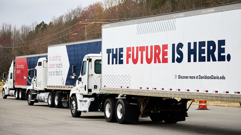 Row of semi-trucks with trailers displaying promotional text messages.