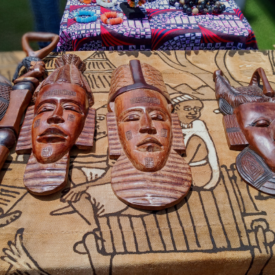 Carved wooden masks on a patterned cloth with beads and accessories in the background.