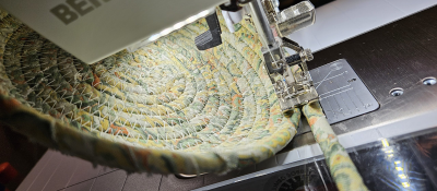 Sewing machine stitching a spiral pattern on coiled fabric.