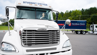 White semi-truck with "Student Driver" sign and Davidson-Davie Community College trailer in the background.