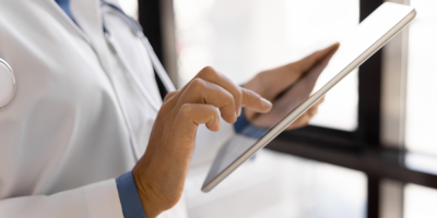 Medical professional using a digital tablet, with a stethoscope visible around their neck.