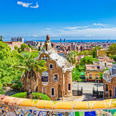 View over Park Güell in Barcelona with a mosaic railing, an ornate building, and the city in the background.